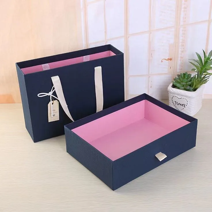 A navy drawer box beside a matching navy carrier bag, both with pale pink linings and ribbon handles