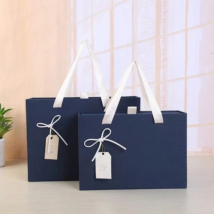 Two navy carrier bags with white ribbon handles and kraft swing tags, standing on a wooden surface