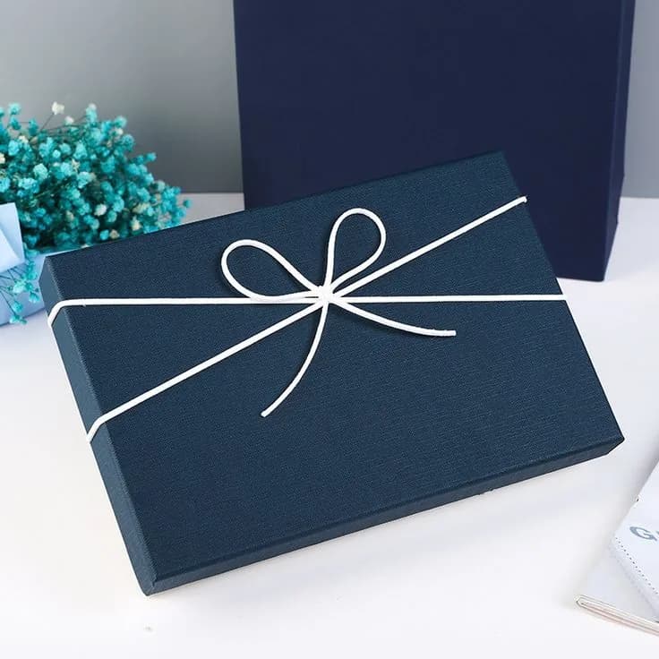 A navy textured lift off lid box tied with a white cord bow, photographed beside dried flowers