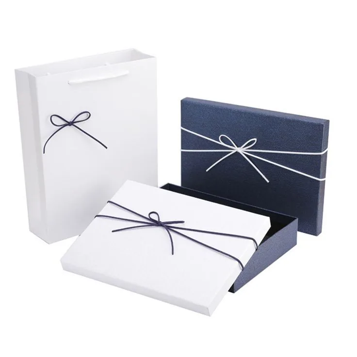 A white gift bag and two lift off lid boxes, one navy and one white, each tied with a contrasting cord bow